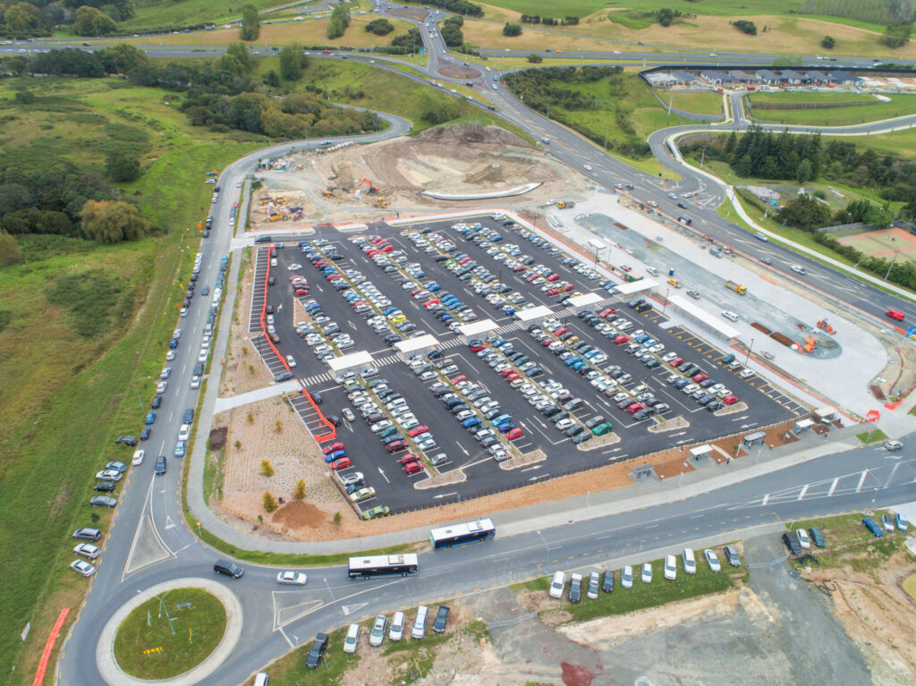 Overhead photo of a carpark full of cars with engineering construction in the background